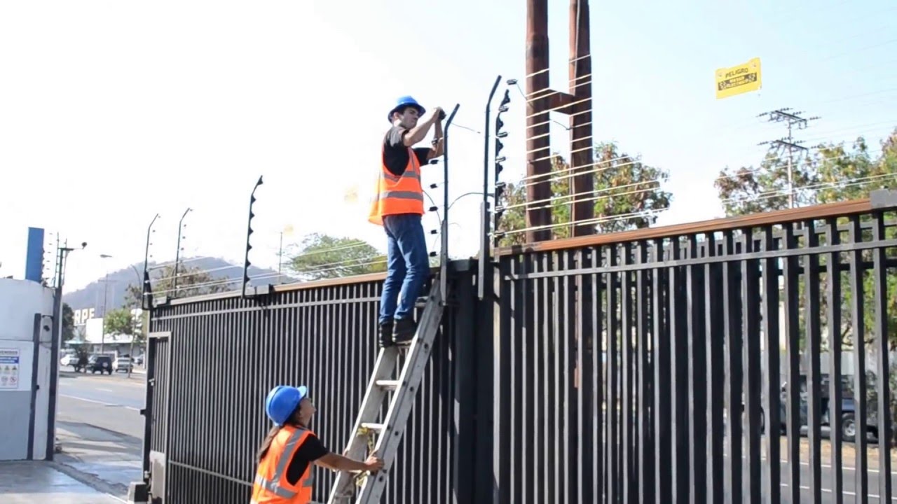 técnicos alarmega realizando mantenimiento instalación de cerca eléctrica y sensores de movimiento en reja metálica corrediza industrial